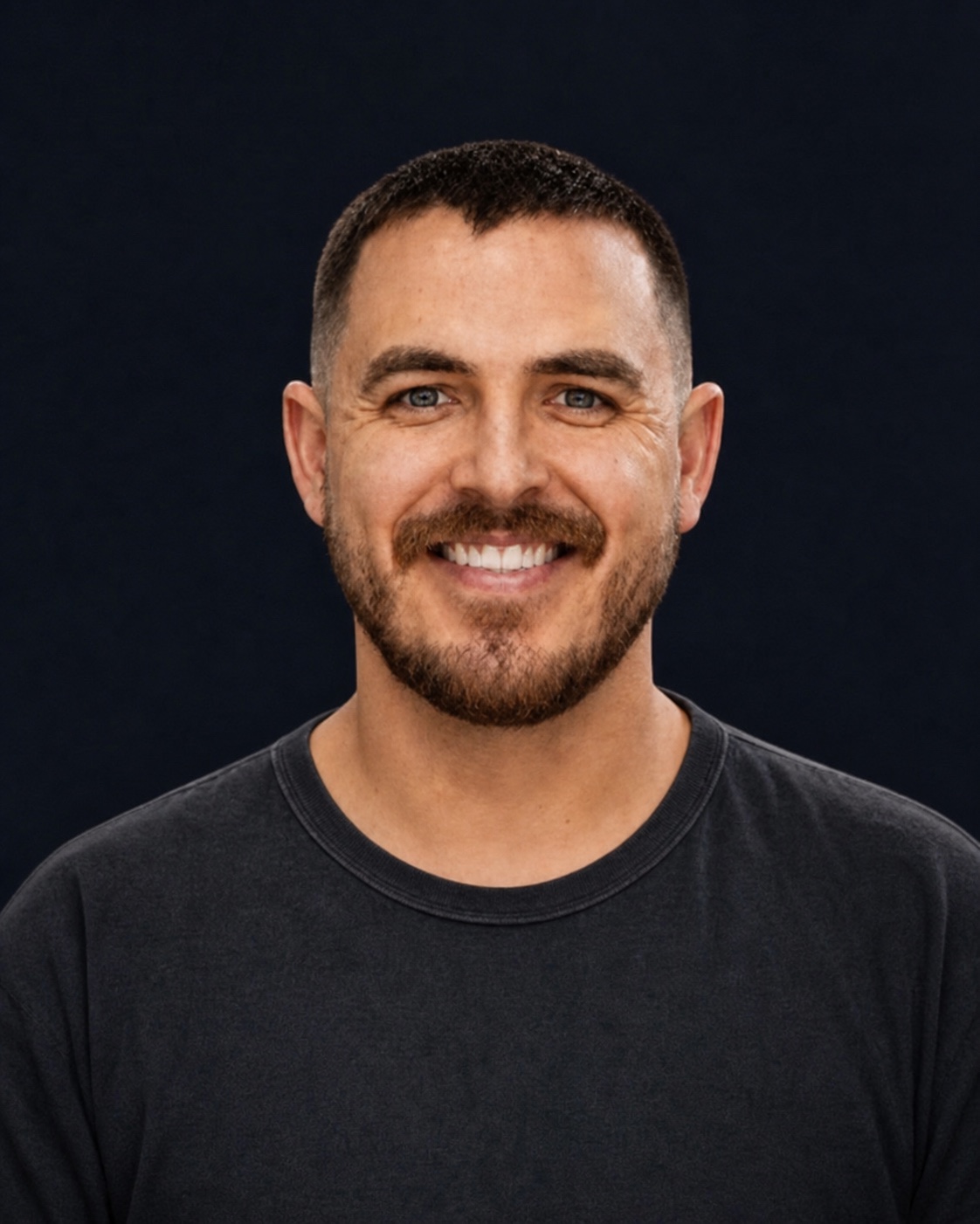 Portrait of Joey smiling in a black crewneck against a dark background.